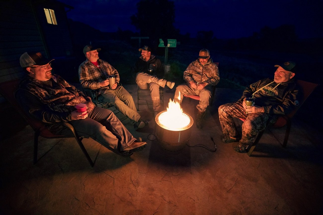 A group of hunters sit around a fire at night.